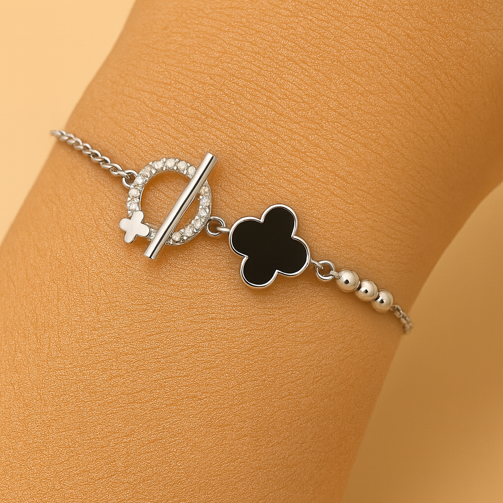 Silver bracelet with black clover charm on a wrist against a beige background
