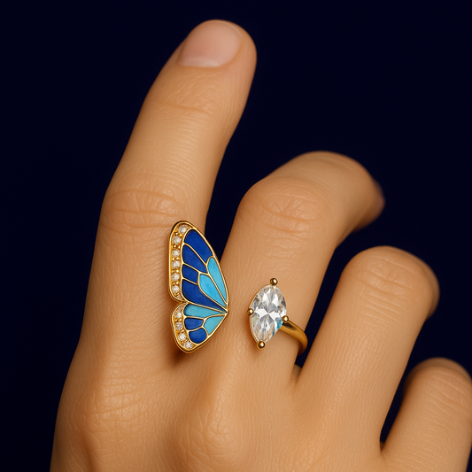 Butterfly-shaped ring with blue wings and gold frame worn on a finger against a black background