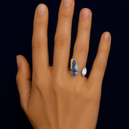Hand wearing a butterfly-shaped ring with blue wings and gold accents on a black background